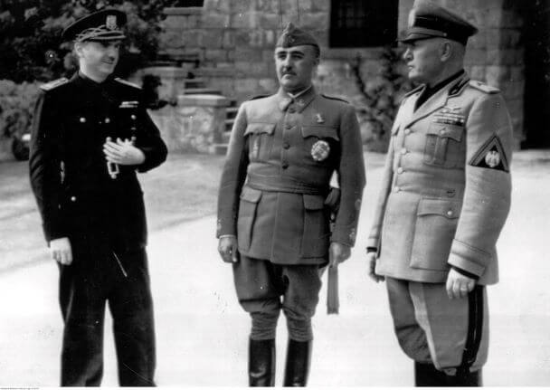 Spotkanie regenta Hiszpanii gen. Francisco Franco z Benito Mussolinim w lutym 1941 roku. Z lewej minister spraw wewnętrznych i zagranicznych Hiszpanii Serrano Suner. Frankistowska Hiszpania – mimo sympatyzowania z Niemcami – zachowała neutralność podczas II wojny, ograniczając się jedynie do wysłania ochotników walczących u boku Wehrmachtu w ZSRR. Być może gdyby Mussolini przyjął taką samą postawę jak gen. Franco, to uchroniłby swój kraj przed porażkami wojennymi i zniszczeniami wywołanymi zarówno przez aliantów, jak i niemieckich sojuszników. Źródło: NAC.