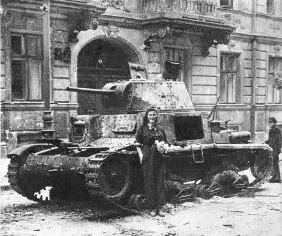 Kurierka Alina Nawrocka przed czołgiem Pz.Kpfw 736(i) – czyli przejętym przez Niemców włoskim M13/40 – zniszczonym przez Powstańców podczas walk o budynek Małej PASTy. 22 sierpnia 1944 roku, Wikimedia, domena publiczna.